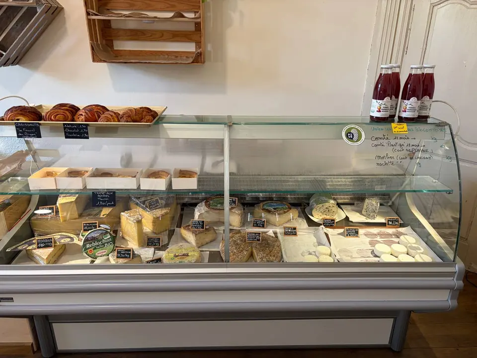 Vitrine réfrigérée de fromages à la coupe, avec des croissants et des pains au chocolat posés au-dessus.